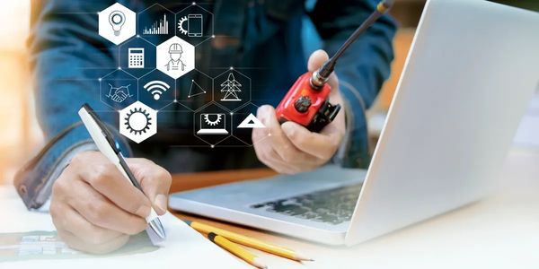 Person using a walkie-talkie and writing notes beside a laptop with digital icons floating.