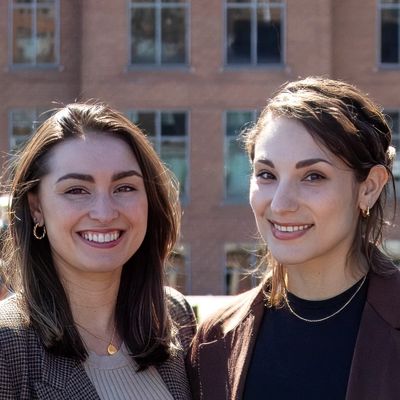 Two smiling women standing outdoors with a building in the background.