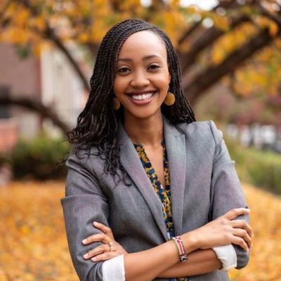 Confident woman smiling outdoors with autumn leaves in background.