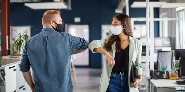A man and a lady wearing medical masks greeting each other using their elbows