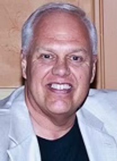 Smiling man with gray hair wearing a light jacket and black shirt.