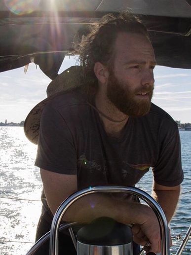 Man with beard steering a boat on a sunny day.