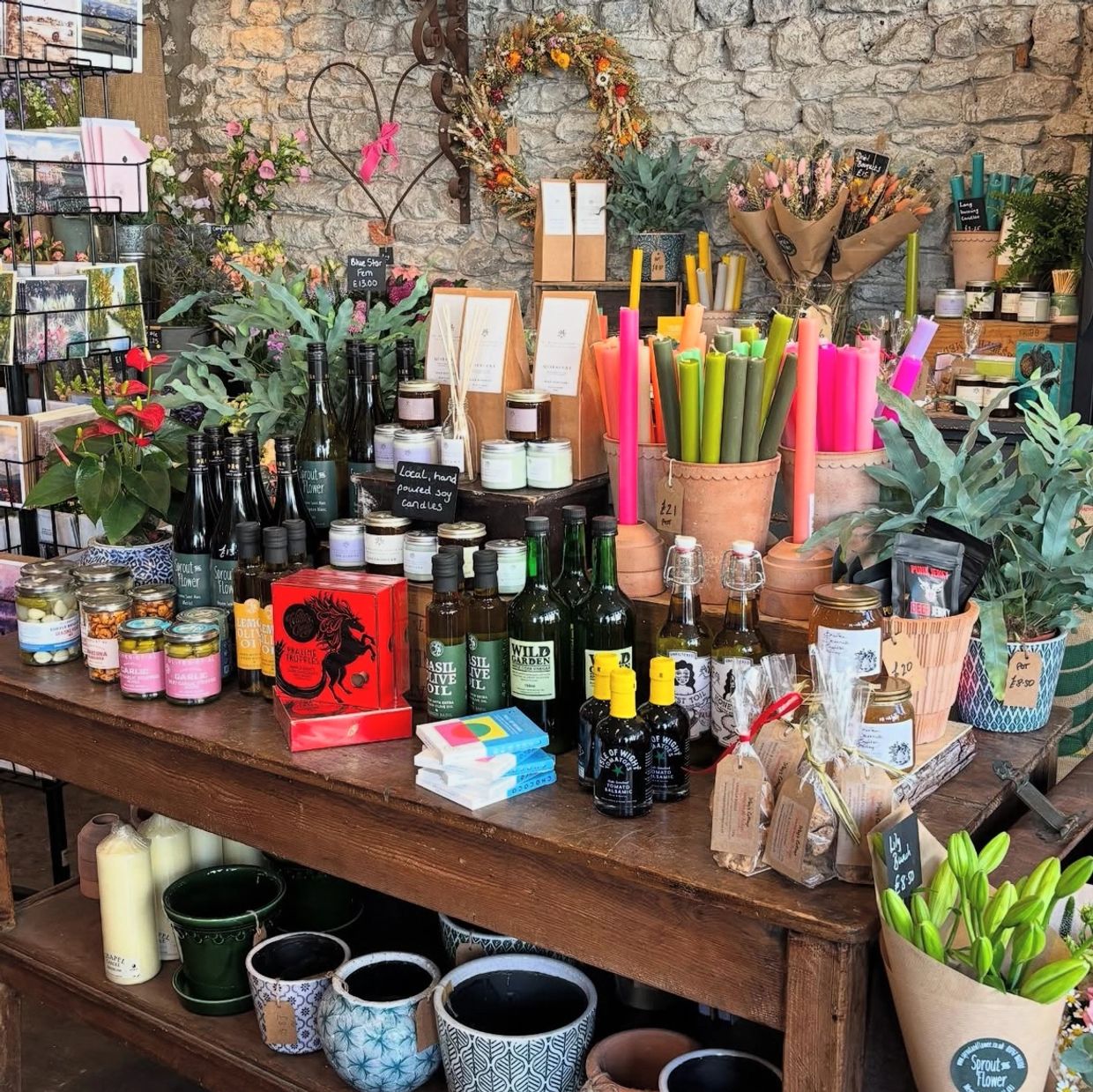A rustic shop display with candles, oils, plants, and gifts on a wooden table.