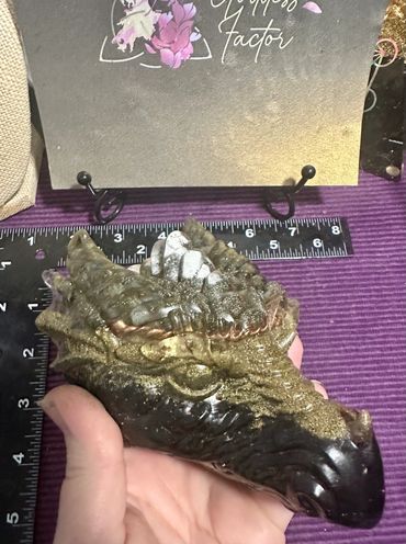 Hand holding a detailed dragon head sculpture with a ruler behind it.