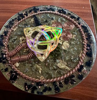 Decorative round object with copper coils and a holographic Celtic knot on a wooden surface.