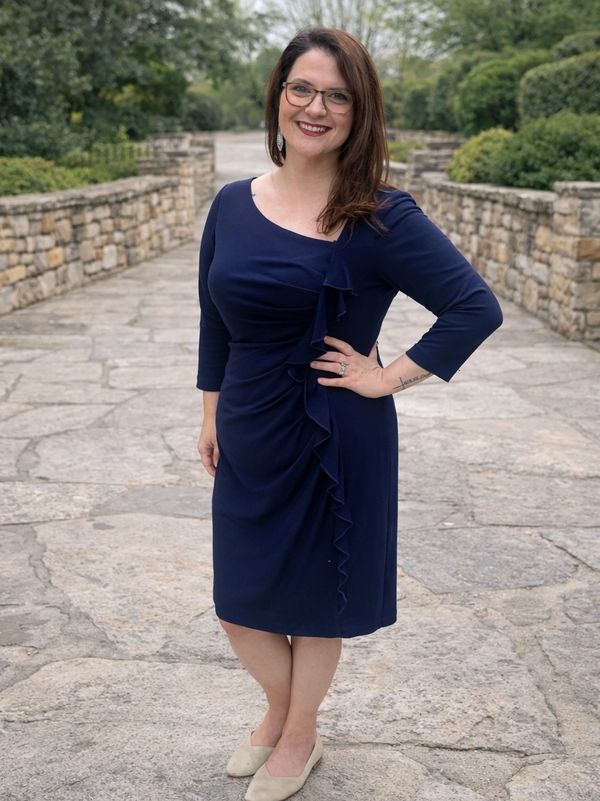 A smiling woman in a navy blue dress posing outdoors on a stone pathway.