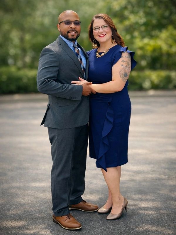 A well-dressed couple posing outdoors, smiling and holding hands.