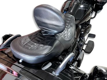 Close-up of a black leather motorcycle seat with backrest and foot pedals.