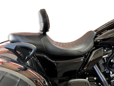 Close-up of a black motorcycle seat with a backrest and part of the frame.