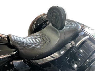 Close-up of a black leather motorcycle seat with backrest on a shiny black bike.
