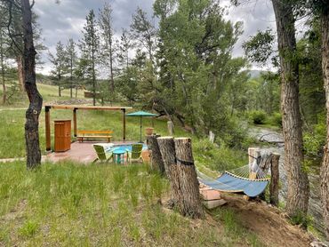 hot spring pool with umbrella on deck and hammock next to the creek in the foreground for self-care