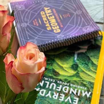 Two coral roses, sacred geometry & everyday mindfulness books on side table for our guests