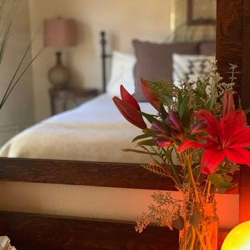 red lilies next to salt lamp in front of mirror reflecting a styled king bed