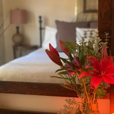 Red lilies next to salt lamp sphere in front of mirror reflecting the styled king bed