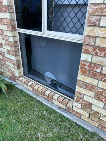 Broken lower window pane in a brick house with grass outside.