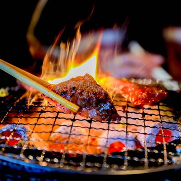 Grilling meat over an open flame with chopsticks on a wire mesh grill.