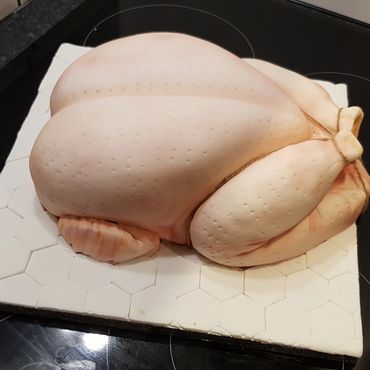 A realistic cake shaped like a raw chicken on a stove.