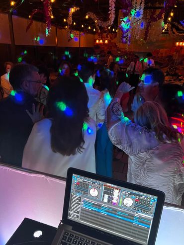 People dancing with colorful lights and DJ laptop in view.