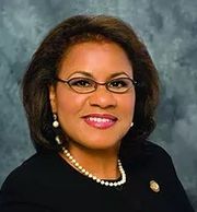 Professional portrait of a smiling woman with glasses and pearl necklace.