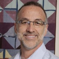 Smiling man with glasses and a beard in front of a quilt.