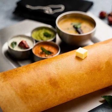 A golden dosa with a butter cube and assorted chutneys on the side.