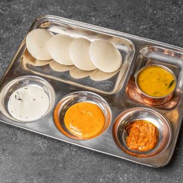 South Indian breakfast with idlis and various chutneys on a stainless steel plate.