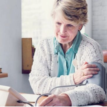 An older woman monitors her blood pressure at home with an arm cuff.
