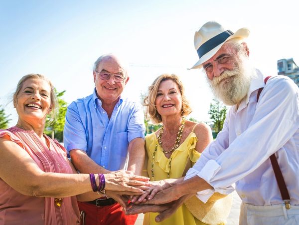 Happy senior friends stacking hands outdoors.