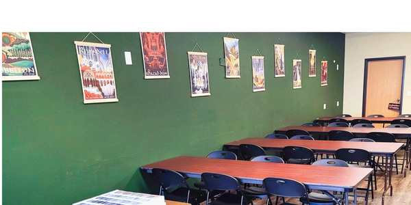 Classroom with tables, chairs, and fantasy-themed posters on a green wall.