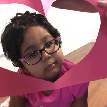 Vedha peeks through a piece of pink paper with a heart cut out.