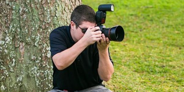 Photographer taking a photo outdoors by a tree.