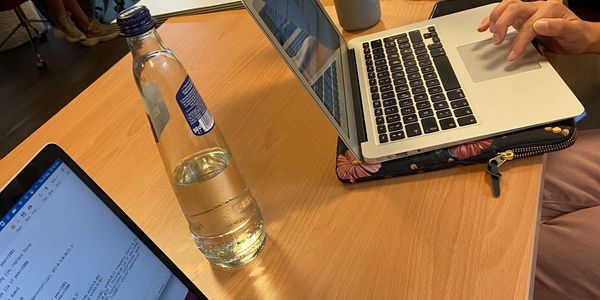 Two laptops and a water bottle on a wooden desk with a person typing.