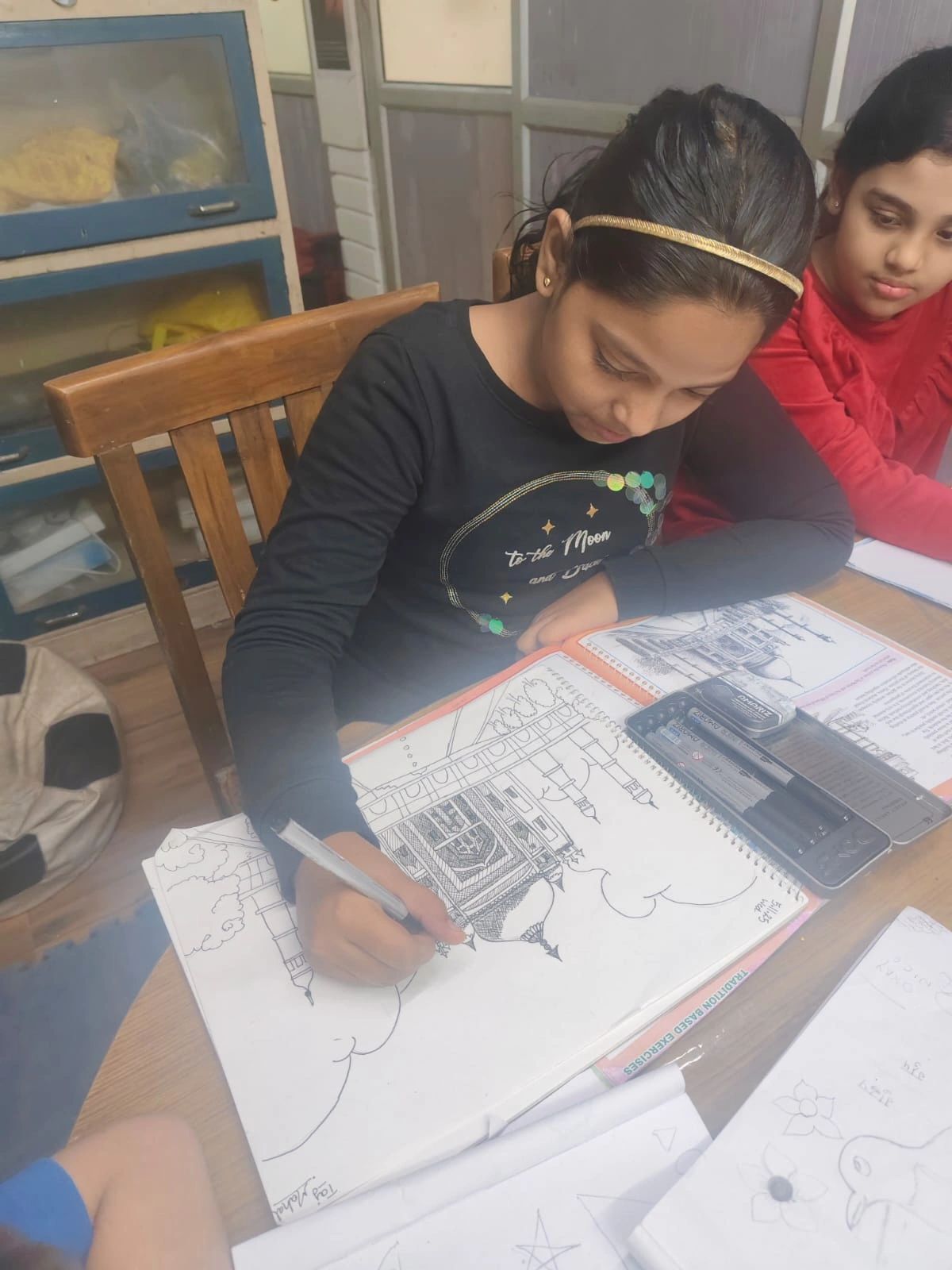 A girl intently drawing a detailed architectural sketch at a table.