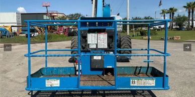 Blue aerial work platform with safety railings in an outdoor industrial area.