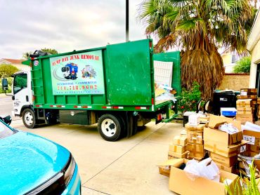 Green junk removal truck and stacked boxes outside a house ready for dump .