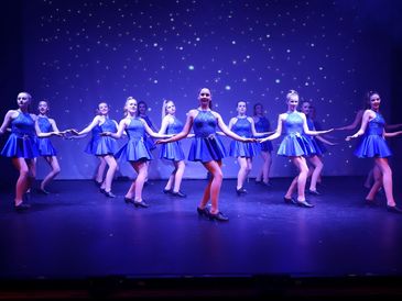 Advanced Tap Dancers on stage wearing a blue sparkly costume and black tap shoes, smiling