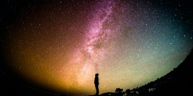 Silhouette of a person gazing at a colorful star-filled night sky.