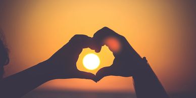 Hands forming a heart shape around the setting sun.