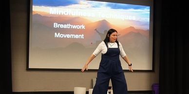 A woman demonstrates mindfulness techniques in front of a presentation screen.