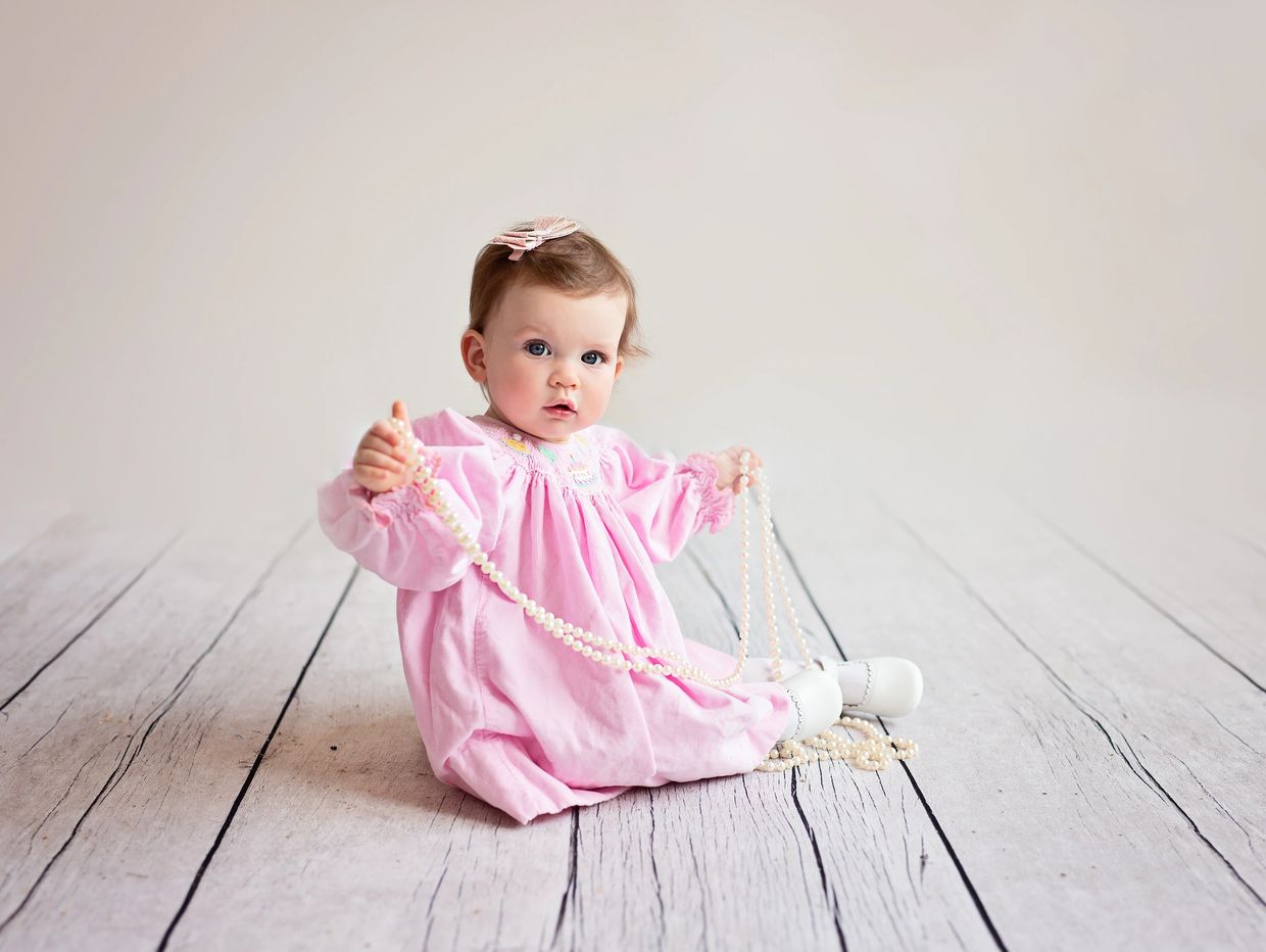 Beautiful baby holding a string of pearls.