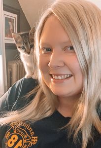 Smiling woman with blonde hair and a curious kitten on her shoulder.