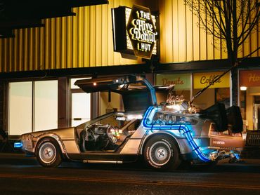 Night time image of the DeLorean Time Machine with the lights, parked in front of The Hive Donut Hut