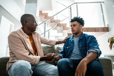A middle-aged black man talking to a black youth. He has a concerned look on his face, and the young