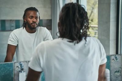 A black man looking at himself in a bathroom mirror.