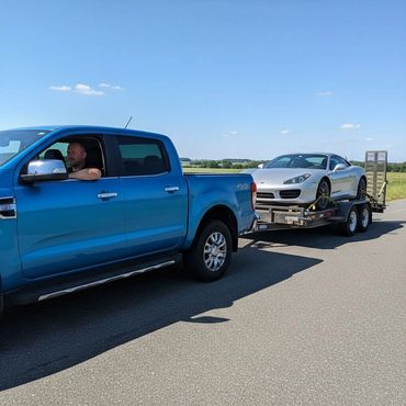 Blue truck towing a silver sports car on a trailer on a sunny day.