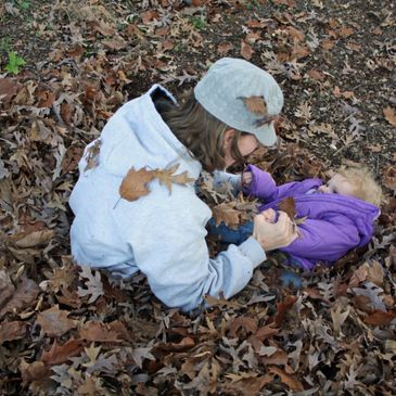 Adult and child playing in autumn leaves, sharing a joyful moment.