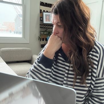 Woman in striped shirt focused on laptop, deep in thought.