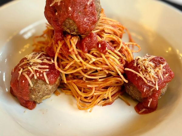Plate of spaghetti with meatballs topped with tomato sauce and cheese.