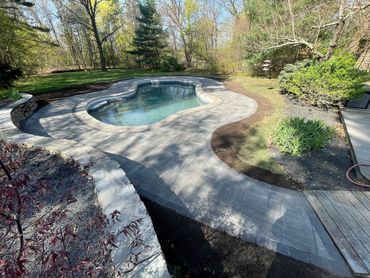 Kidney-shaped pool with stone patio and surrounding greenery.