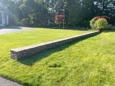 Stone wall in a sunny garden with green grass.
